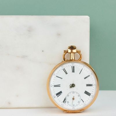 montre de poche en or avec des chiffres romains, posée sur un bloc de marbre