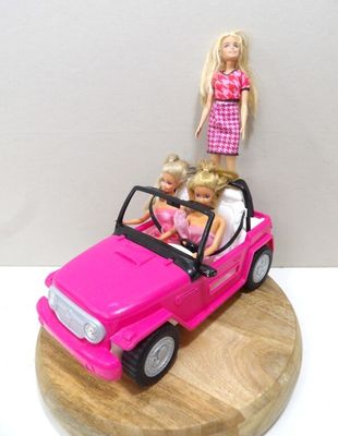 une petite voiture rose avec une poupée Barbie assise dessus