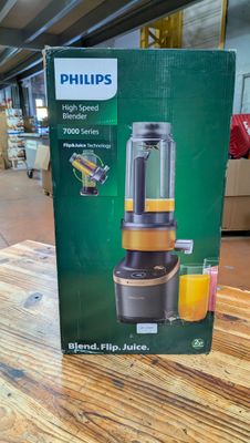 Mixeur Philips dans son emballage, posé sur une table en bois, avec un verre de jus d'orange à côté