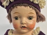 a close up of a doll wearing a purple dress and a purple hat