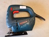 a corded jig saw on the floor next to a piece of wood