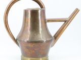 an old copper watering can with a wooden handle on a white background