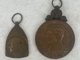 two small bronze medals of a man and a woman on a white surface