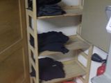 a wooden shelf with clothes on it next to a refrigerator