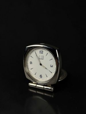 a small silver clock sitting on a black surface
