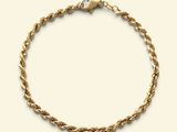 a close up of a gold rope bracelet on a white background
