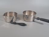 two silver pots and a spoon sitting on a table