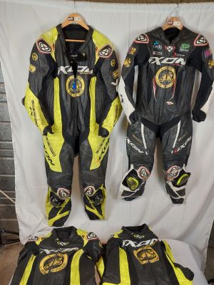 Trois combinaisons de moto sont alignées sur une table devant un fond blanc.