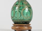 un œuf en verre vert posé sur un socle en bois, sur une surface blanche