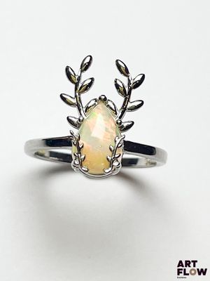 un gros plan d'une bague ornée d'une pierre oplite entourée de feuilles