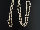 un collier de perles blanches avec un fermoir en or sur fond noir