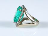 a close up of an emerald and diamond ring on a white surface