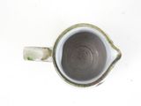 a white and green cup with a handle on a white table