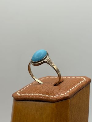 une image représentant une bague ornée d'une pierre turquoise posée sur une boîte en bois
