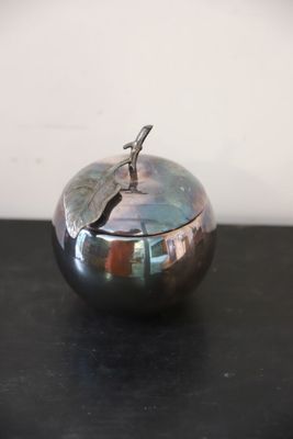 une pomme argentée ornée d'une feuille, posée sur une table