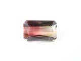 un gros plan d'une tourmaline rose facettée posée sur une surface blanche