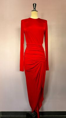La robe rouge est posée sur un présentoir à mannequin devant un mur blanc.