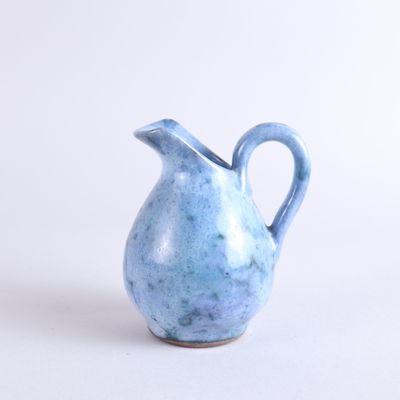 a small blue vase with a handle on a white surface