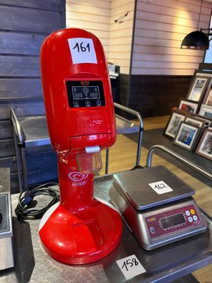 une machine rouge posée sur une table, à côté d'une balance
