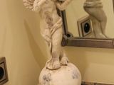 une statue représentant un Cupidon, posée sur un socle devant un miroir