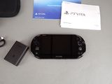 a black sony vita next to a charger and a wallet