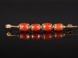 une broche composée de perles dorées et corail sur un fond noir