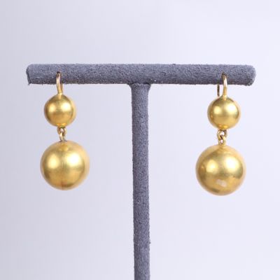 a pair of gold ball earrings on a stand