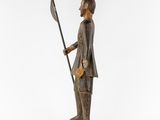 a wooden statue of a man holding a spear and a flag