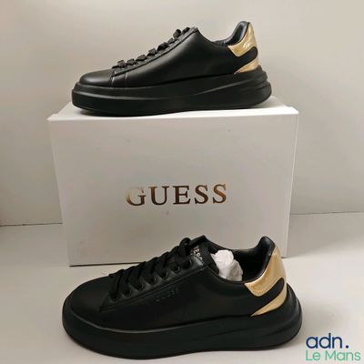 une paire de chaussures noires et dorées sur lesquelles est inscrit le mot « Guess »