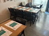 Des tables et des chaises sont alignées dans une pièce où sont accrochés des tableaux aux murs.