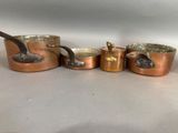 four copper pots and pans are lined up on a table