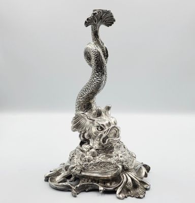 une statue en argent représentant un poisson posé sur un rocher, avec une queue de poisson