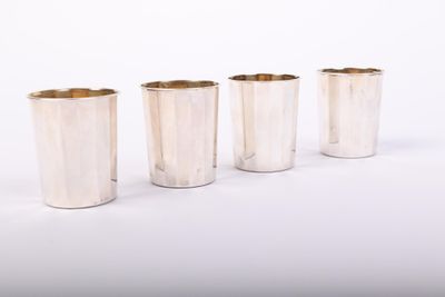 four silver cups are lined up in a row on a white surface