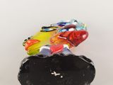 multicolored glass frog figurine sitting on a rock on a white surface
