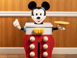 a mickey mouse toy standing on the floor with a frisbee in his hand