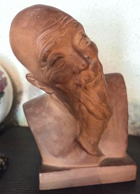 un buste d'homme barbu posé sur une table, à côté d'un vase