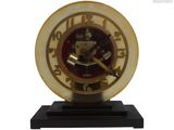 une horloge dorée posée sur un socle noir, sur fond blanc