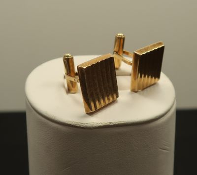 a close up of a pair of gold cufflinks on a white stand