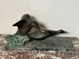 une statue en bronze représentant un canard, posée sur un socle en marbre
