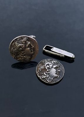 a silver coin and a silver tie bar on a black surface