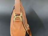 tan leather handbag with gold hardware and strap on a black background