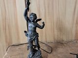 une petite statue représentant un garçon tenant une lampe, posée sur une table