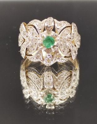 une photo d'une bague sertie d'un diamant et d'une émeraude, posée sur une surface réfléchissante