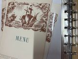 a menu book on a table next to a cup of coffee