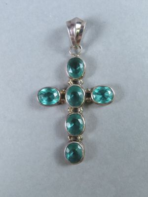 un pendentif en forme de croix orné de pierres vertes sur fond blanc