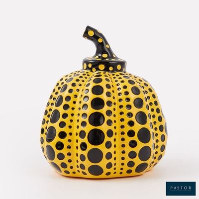 une citrouille à pois jaunes et noirs posée sur une surface blanche