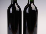 two bottles of red wine sitting next to each other on a white surface