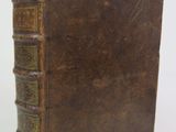 an old brown book sitting on top of a table next to a white wall