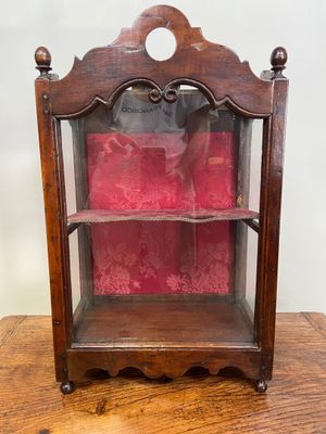 une vieille vitrine en bois surmontée d'un coussin rouge