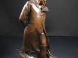 statue en bronze représentant un homme coiffé d'un chapeau et vêtu d'un manteau, assis sur un rocher